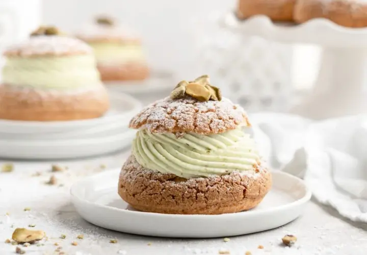 Un délice aérien : une religieuse garnie d'une crème onctueuse à la pistache, saupoudrée de sucre glace et décorée de pistaches.