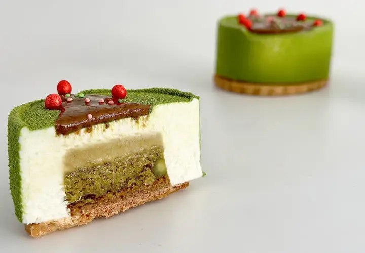 Entremet pistache aux couches délicates de mousse blanche, de crémeux et de biscuit croustillant, décoré de fruits rouges.