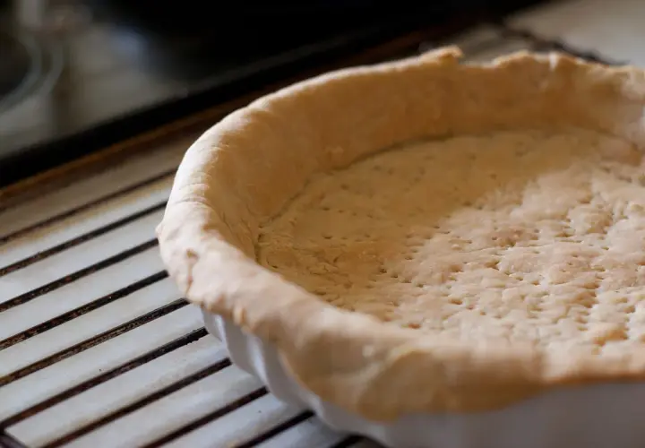 Pâte brisée crue dans un moule, prête à être garnie. Attention à la péremption de la pâte brisée pour une cuisson parfaite.