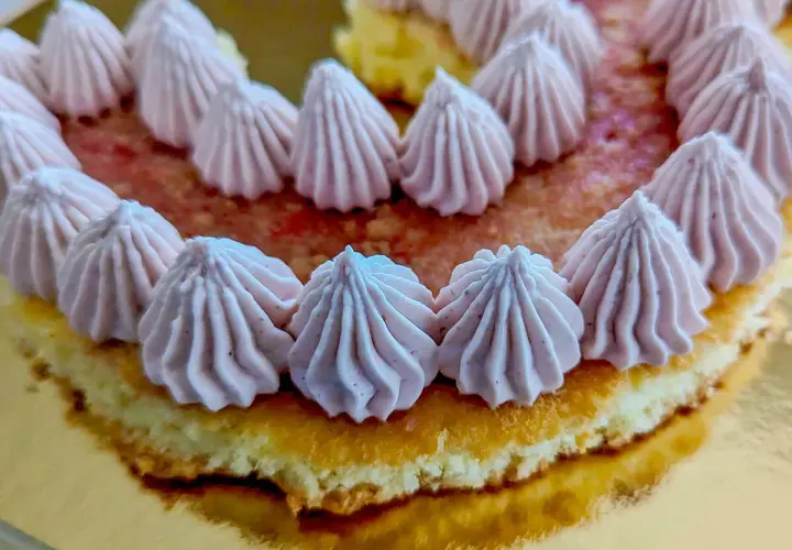 Gâteau rond décoré de rosaces de ganache framboise sur un lit de fruits rouges.
