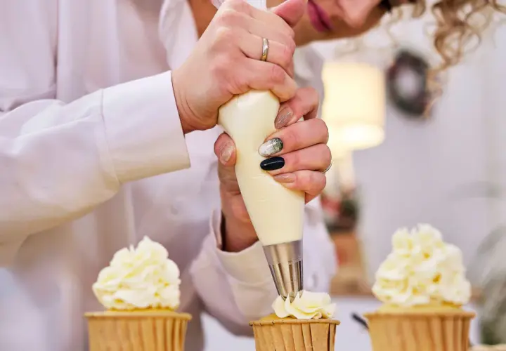 Une pâtissière décore des cupcakes avec une chantilly mascarpone aérienne.