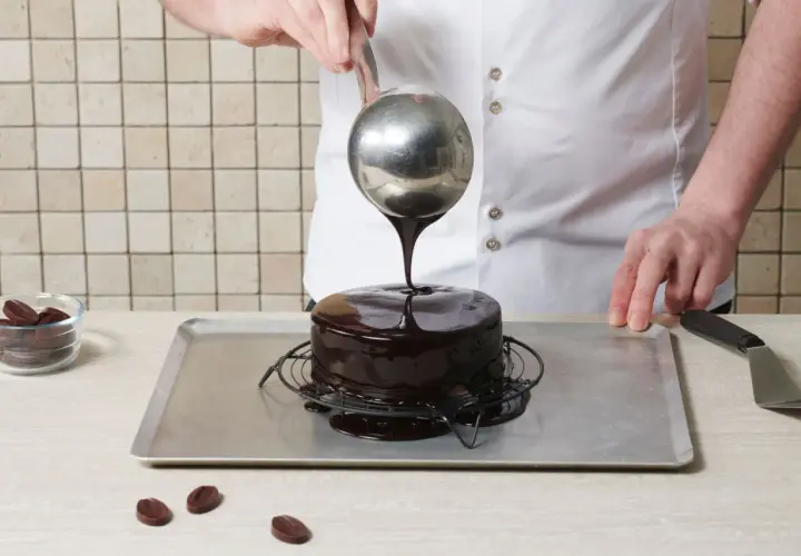 Un chef verse un glaçage au chocolat brillant sur un gâteau, créant le meilleur glaçage pour décorer un gâteau.