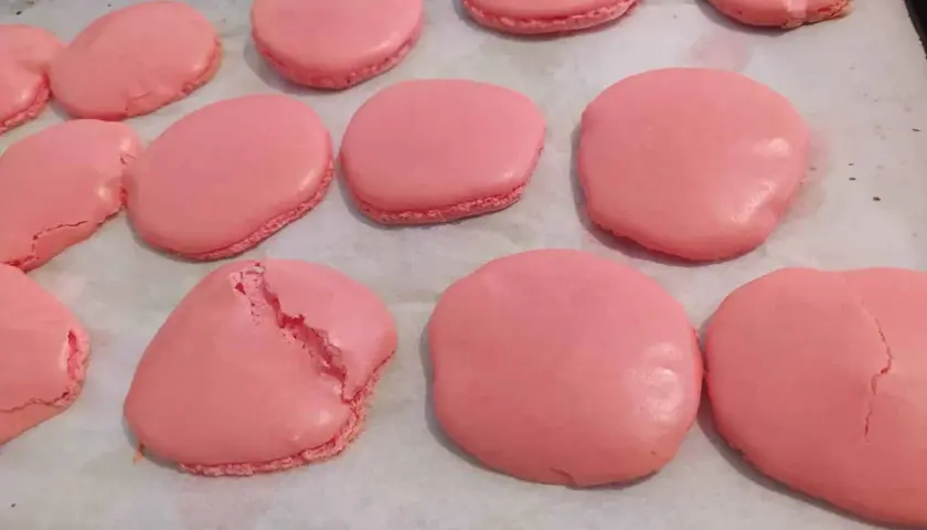 Des macarons roses sur une plaque de cuisson. Certains sont craquelés, un mystère pour comprendre pourquoi mes macarons craquent.