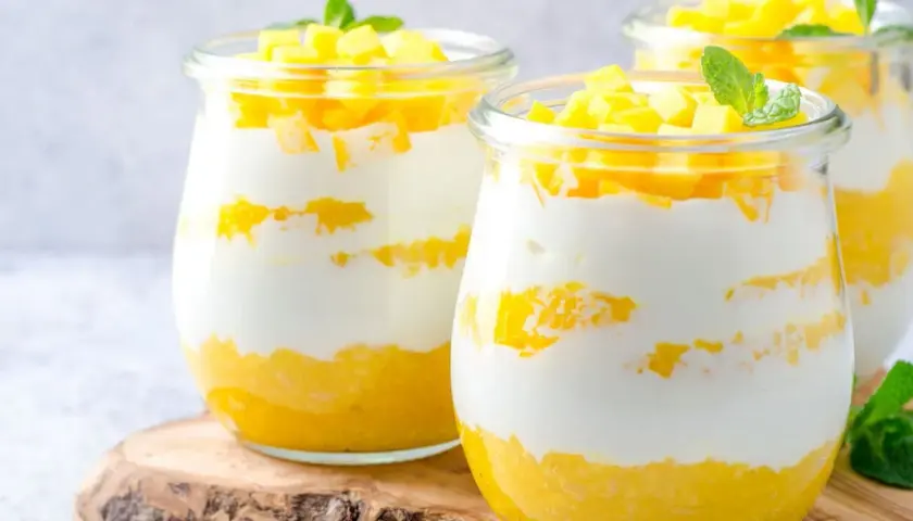 Délicieux dessert printemps en verrine, alternant couches de yaourt crémeux et de mangue fraîche, garni de dés de mangue et d'une feuille de menthe.