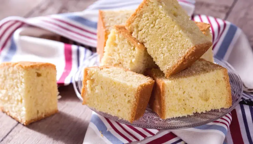 Tranches de madeira cake dorées et moelleuses, empilées sur une assiette en verre, avec une serviette rayée.