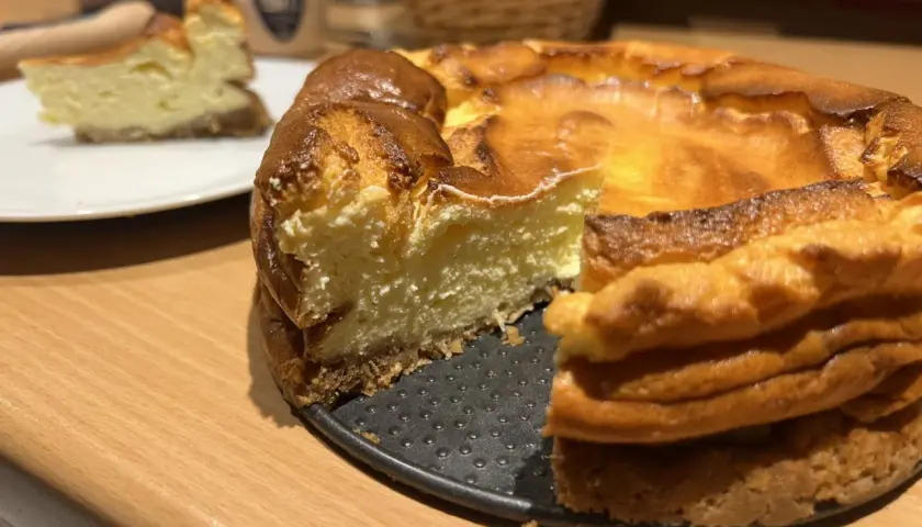 Un délicieux gâteau healthy, un cheesecake doré et crémeux, avec une part déjà servie sur une assiette blanche.