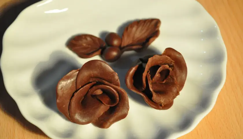 Deux roses et une petite branche avec des baies, le tout en chocolat plastique, sur une assiette blanche.