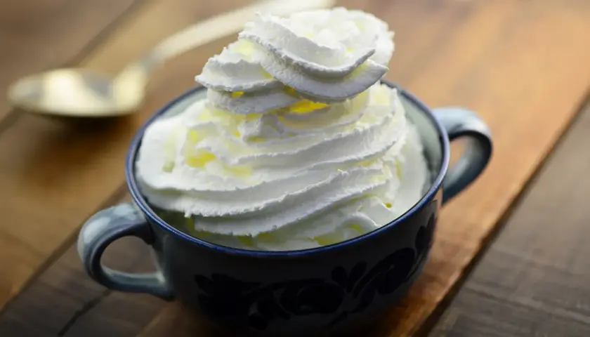 Une tasse bleue remplie de chantilly maison, prête à être dégustée avec une cuillère dorée en arrière-plan.
