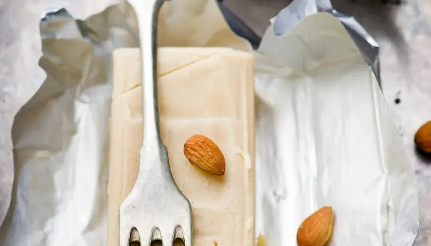 Bloc de pâte d'amande pour recouvrir un gâteau, avec une fourchette et des amandes.
