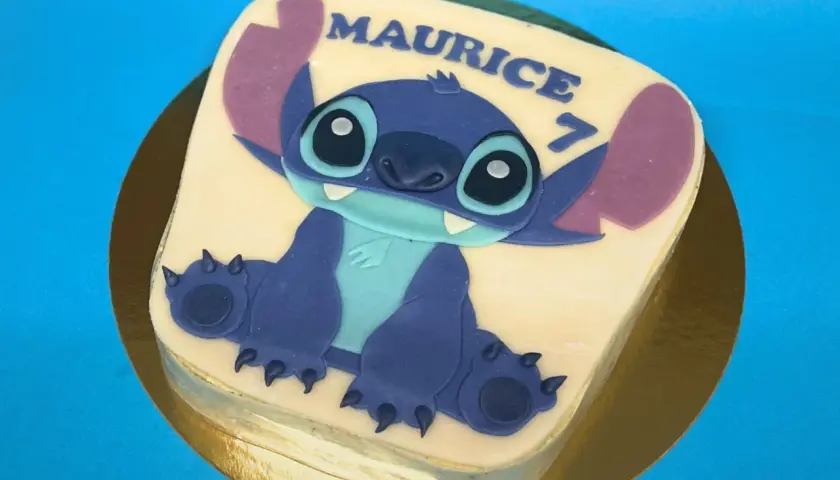 Gâteau thème Stitch pour Maurice, qui fête ses 7 ans. Le personnage bleu est assis sur un glaçage blanc.