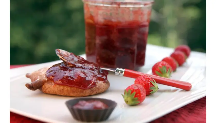 Confiture de framboise pectine sur un biscuit, avec des fraises fraîches alignées.