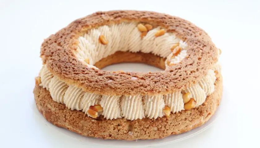 Un Paris-Brest rond, garni d'une crème onctueuse et parsemé de morceaux de praliné cacahuète croquant.