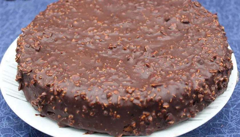 Gâteau rond au chocolat avec un glaçage rocher croustillant parsemé de noisettes concassées. Un délice gourmand.