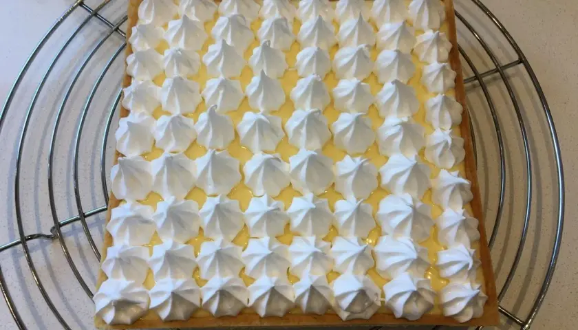 Tarte citron meringuée rectangulaire, garnie de crème citron et de petites meringues blanches disposées en grille. Un délice signé Pierre Hermé.