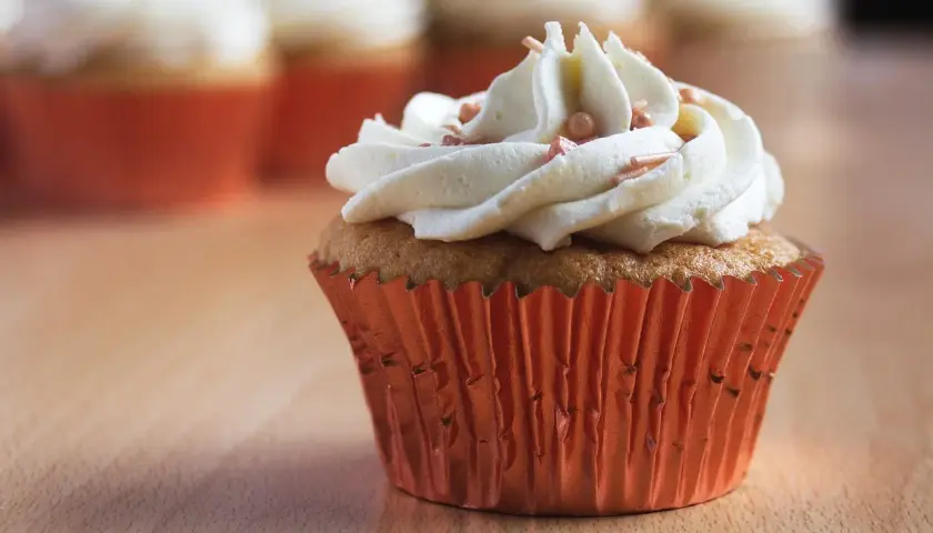 Un cupcake orné d'une généreuse ganache chocolat blanc, parsemé de perles rosées, dans un élégant caissette orange.