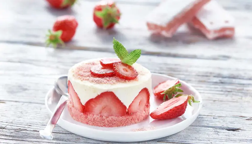 Délicieux gâteau biscuit aux fraises, garni de crème et de fruits frais, sur une assiette blanche avec des fraises éparpillées.