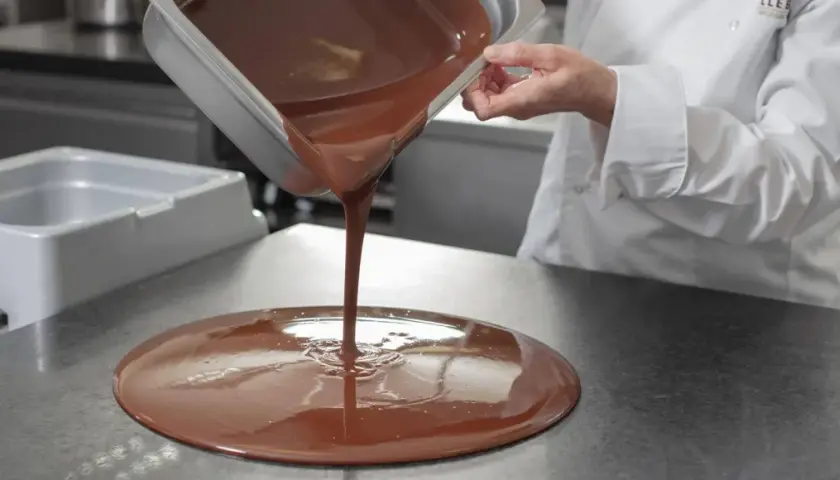Un chef verse du chocolat fondu, illustrant la différence entre le beurre de cacao et le mycryo pour un tempérage parfait.