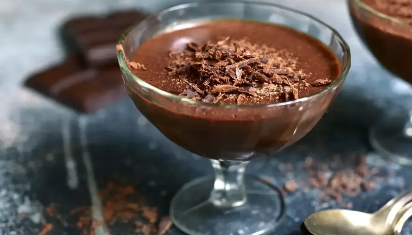 Délicieuse mousse chocolat entremet, garnie de copeaux de chocolat, servie dans un verre. Des carrés de chocolat sont flous en arrière-plan.