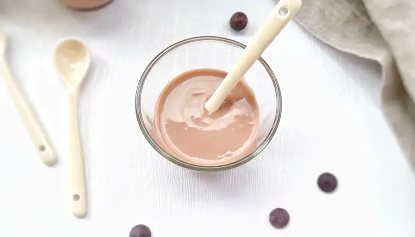 Un bol de ganache praliné onctueuse, prêt à être dégusté avec une cuillère. Quelques pépites de chocolat parsèment la table.