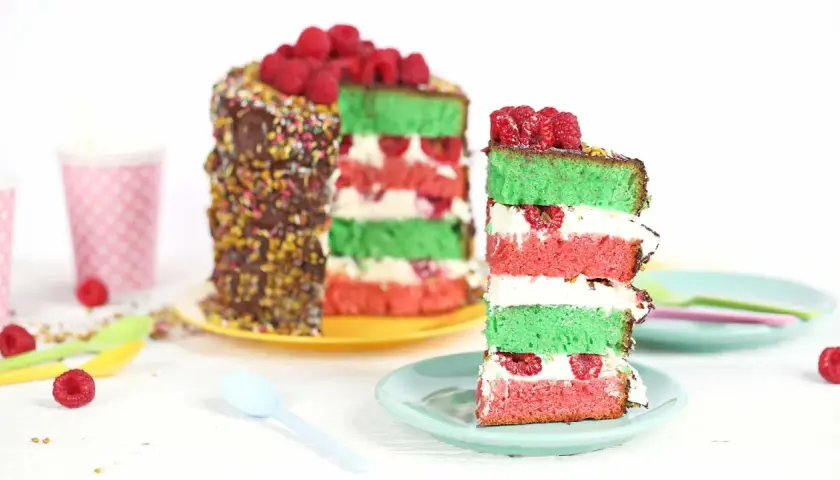 Gâteau coloré aux couches de pistache et framboise, garni de fruits rouges frais.