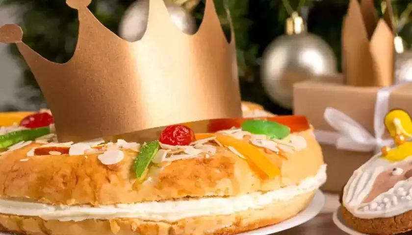 Un roi porte une couronne dorée sur un délicieux gâteau praliné, décoré de fruits confits et d'amandes. Un cadeau emballé et des décorations de Noël en arrière-plan.