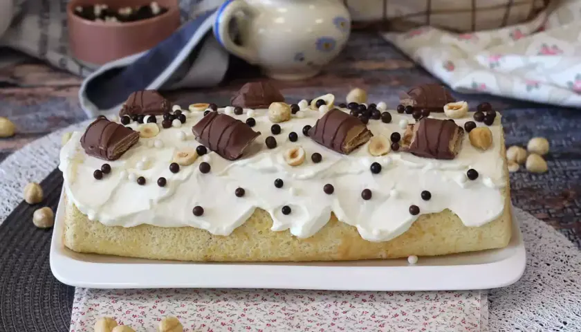 Gâteau moelleux recouvert de crème fouettée, décoré de morceaux de Kinder Bueno, noisettes et billes chocolatées. Un délice gourmand !