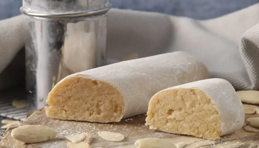 Pâte d'amande, c'est quoi ? Deux rouleaux de massepain, saupoudrés de sucre glace, sur une planche en bois, entourés d'amandes effilées.