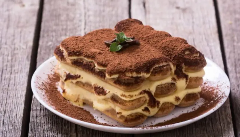 Un délicieux tiramisu, dont l'origine italienne est évidente, saupoudré de cacao, sur une assiette blanche.