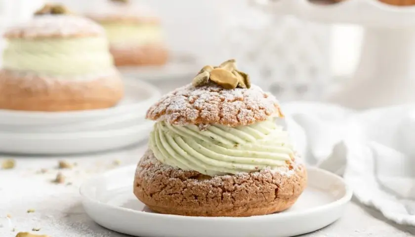 Un délice aérien : une religieuse garnie d'une crème onctueuse à la pistache, saupoudrée de sucre glace et décorée de pistaches.