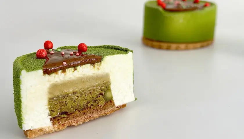 Entremet pistache aux couches délicates de mousse blanche, de crémeux et de biscuit croustillant, décoré de fruits rouges.