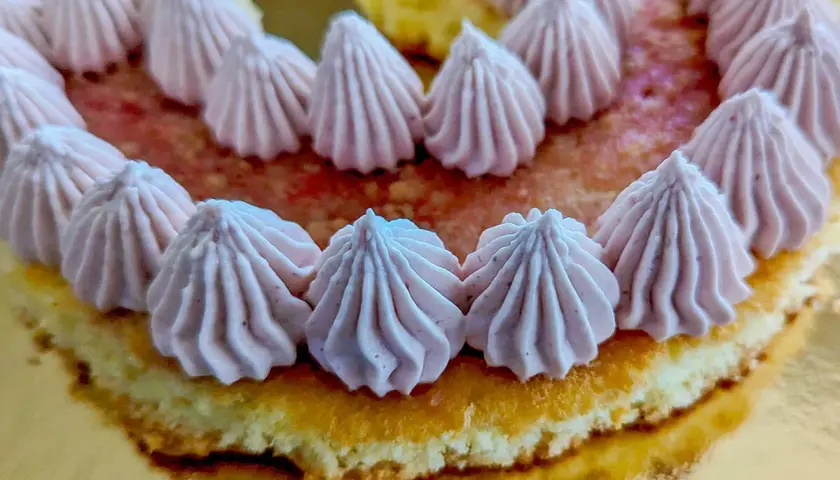 Gâteau rond décoré de rosaces de ganache framboise sur un lit de fruits rouges.