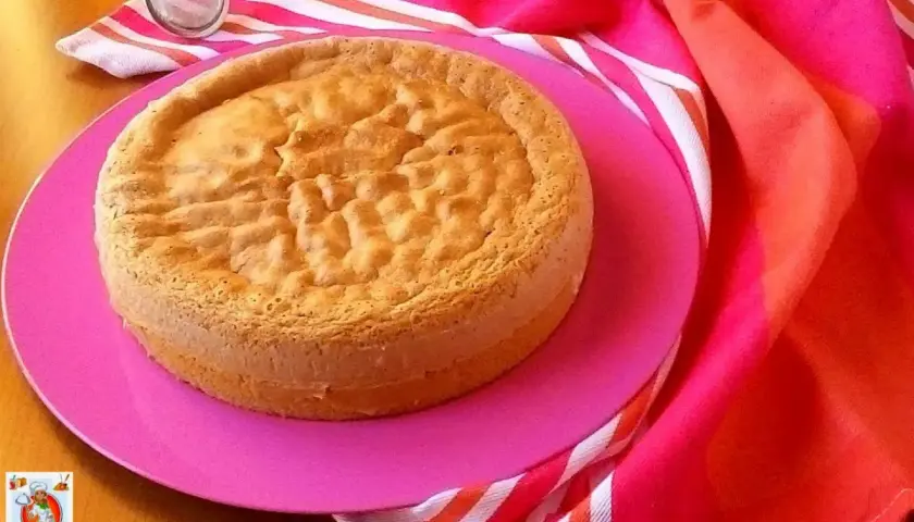 Un gâteau "Pan di Spagna" sur une assiette rose, prêt pour la conservation génoise. Un tamis est à côté.