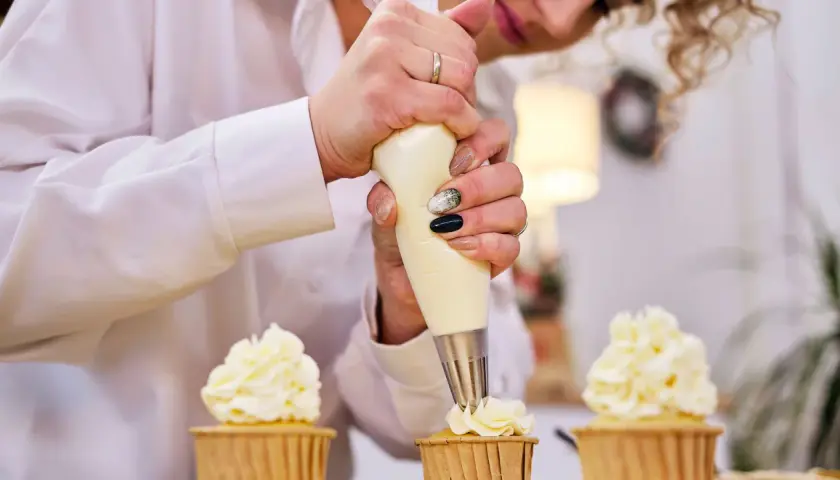 Une pâtissière décore des cupcakes avec une chantilly mascarpone aérienne.