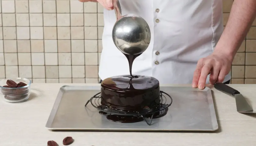 Un chef verse un glaçage au chocolat brillant sur un gâteau, créant le meilleur glaçage pour décorer un gâteau.