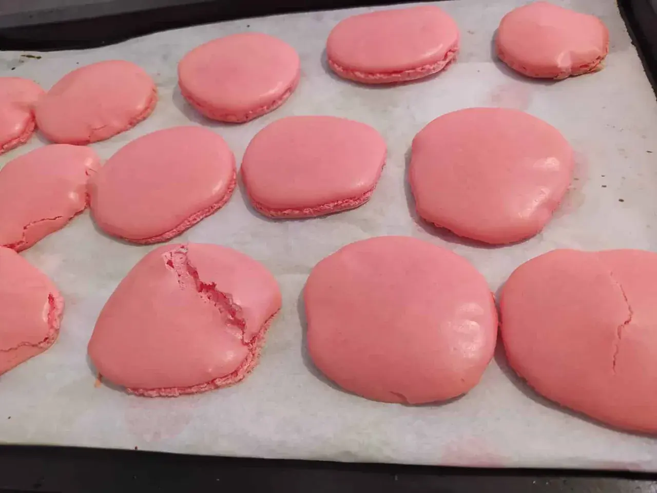 Des macarons roses sur une plaque de cuisson. Certains sont craquelés, un mystère pour comprendre pourquoi mes macarons craquent.