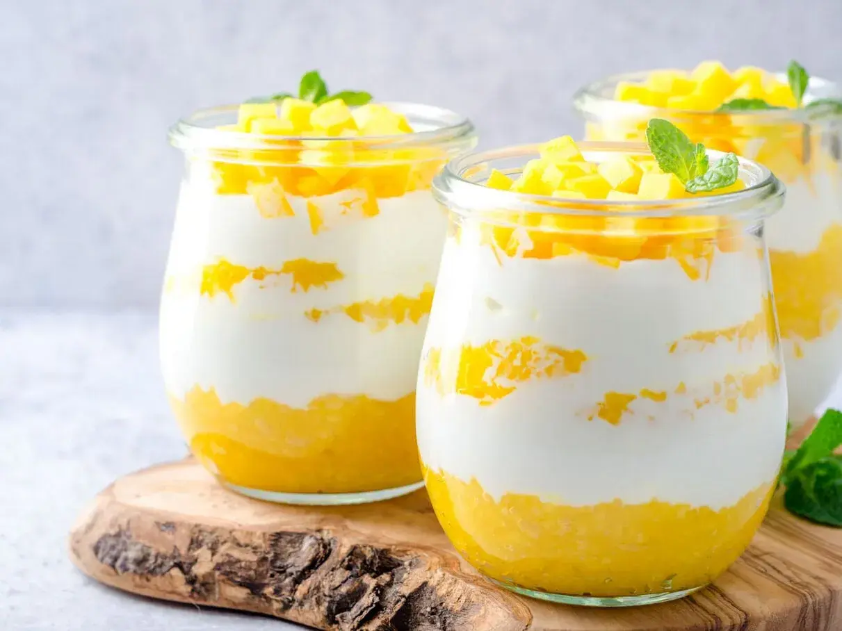 Délicieux dessert printemps en verrine, alternant couches de yaourt crémeux et de mangue fraîche, garni de dés de mangue et d'une feuille de menthe.