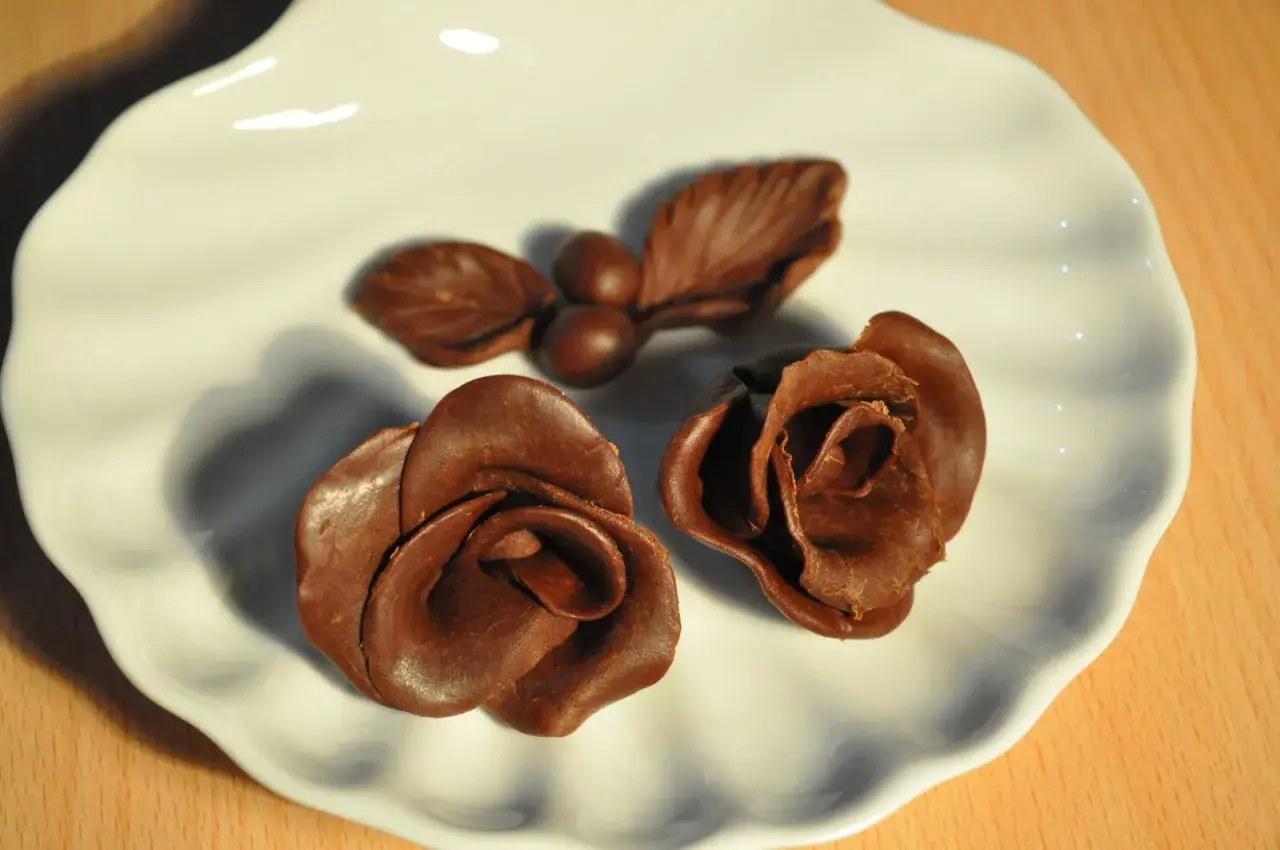 Deux roses et une petite branche avec des baies, le tout en chocolat plastique, sur une assiette blanche.