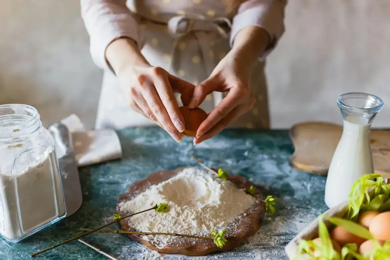 Mains préparant un œuf pour des ingrédients de pâtisserie. Farine, lait et œufs sont prêts pour la création d'une recette.