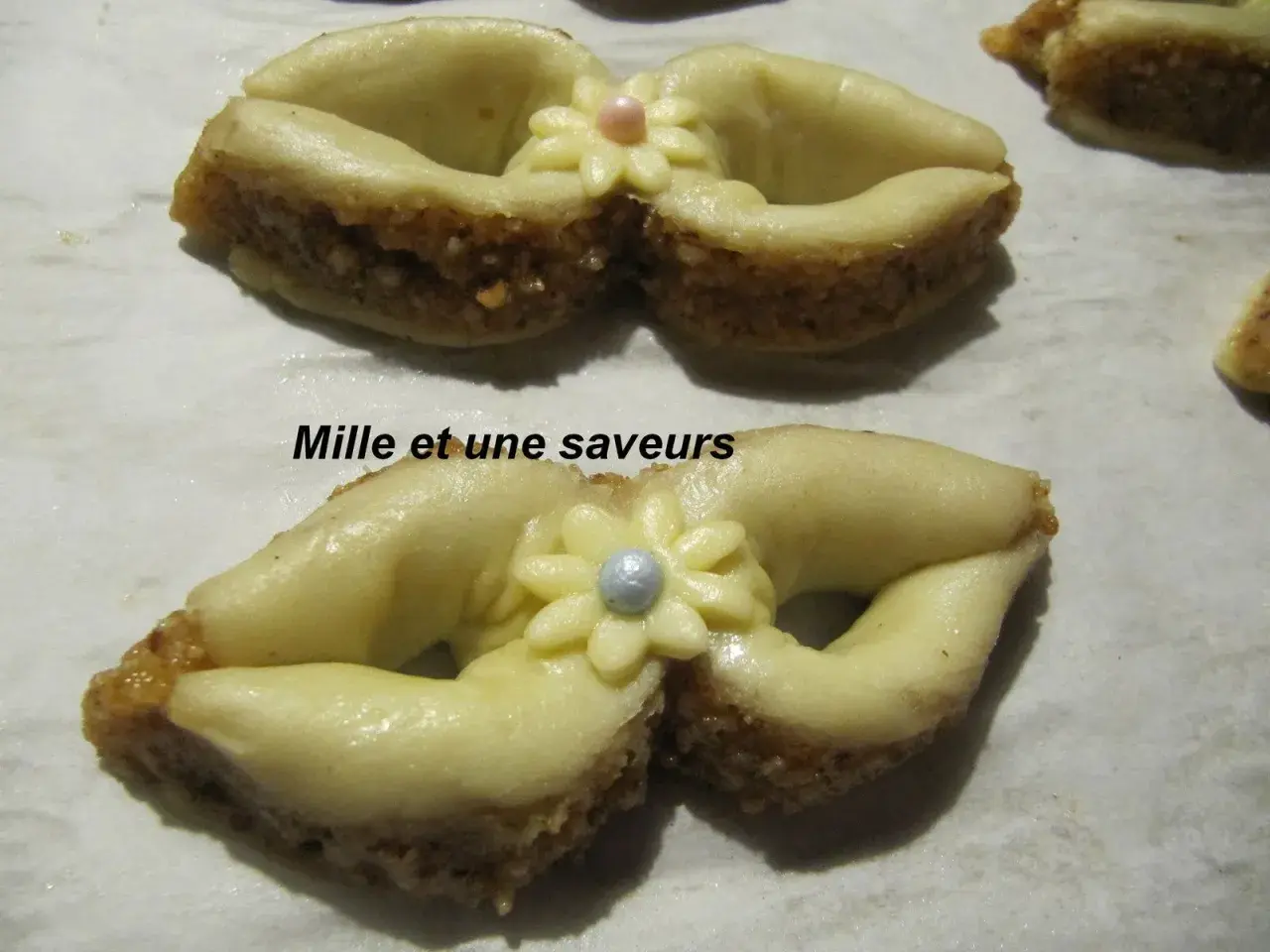 Délicieux noeud en pâte à sucre, orné d'une fleur et d'une perle, sur un lit de biscuits aux amandes.
