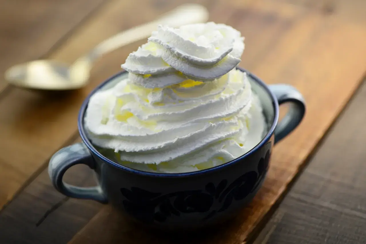 Une tasse bleue remplie de chantilly maison, prête à être dégustée avec une cuillère dorée en arrière-plan.