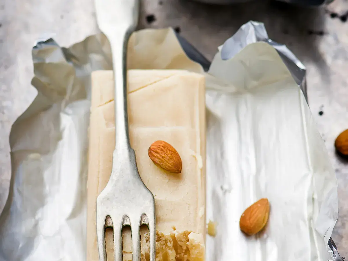 Bloc de pâte d'amande pour recouvrir un gâteau, avec une fourchette et des amandes.