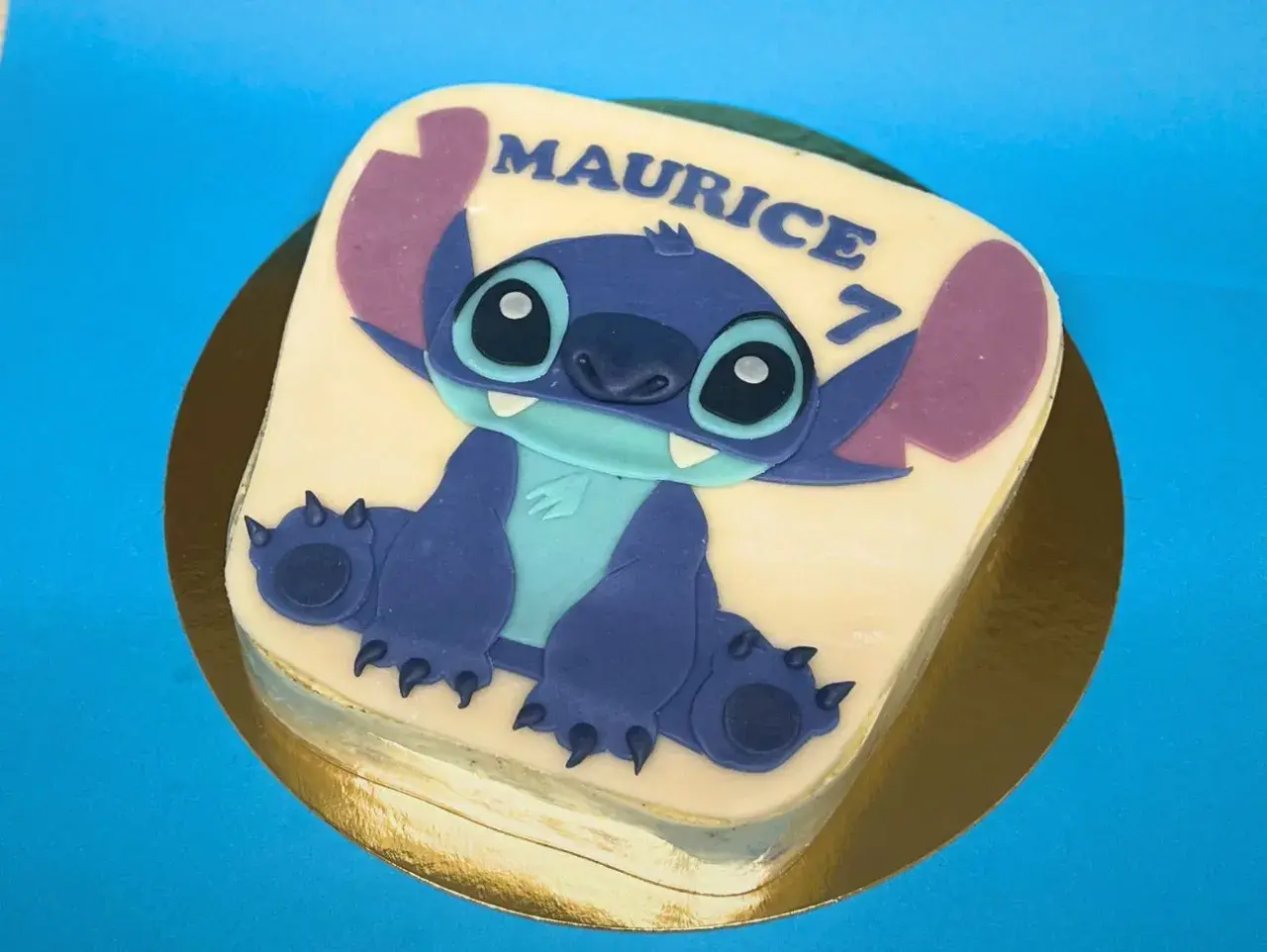 Gâteau thème Stitch pour Maurice, qui fête ses 7 ans. Le personnage bleu est assis sur un glaçage blanc.