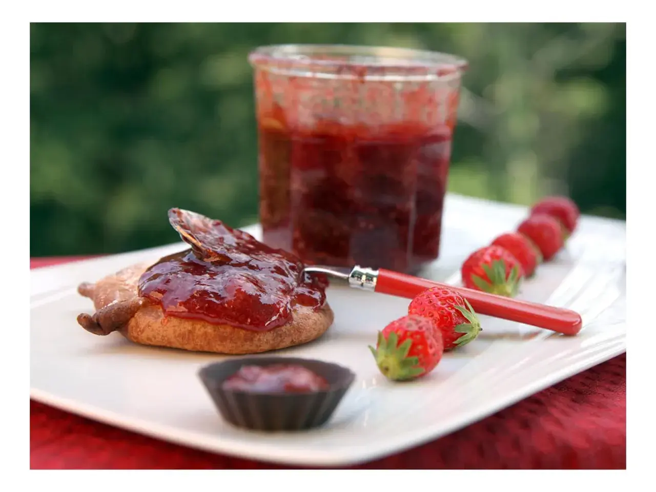 Confiture de framboise pectine sur un biscuit, avec des fraises fraîches alignées.
