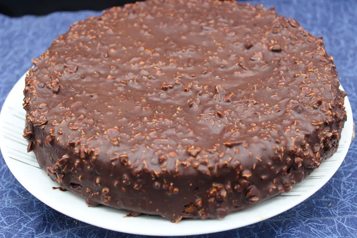 Gâteau rond au chocolat avec un glaçage rocher croustillant parsemé de noisettes concassées. Un délice gourmand.