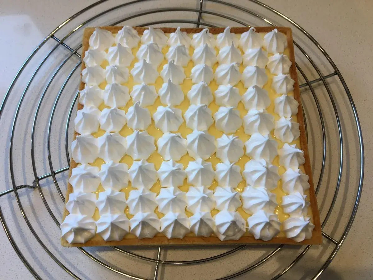 Tarte citron meringuée rectangulaire, garnie de crème citron et de petites meringues blanches disposées en grille. Un délice signé Pierre Hermé.