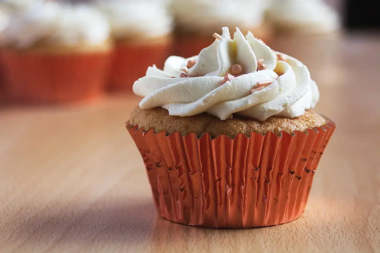 Un cupcake orné d'une généreuse ganache chocolat blanc, parsemé de perles rosées, dans un élégant caissette orange.