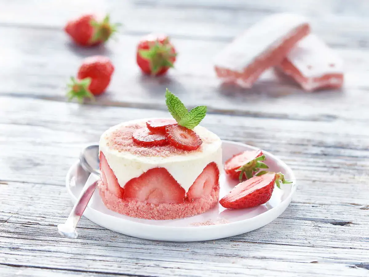 Délicieux gâteau biscuit aux fraises, garni de crème et de fruits frais, sur une assiette blanche avec des fraises éparpillées.