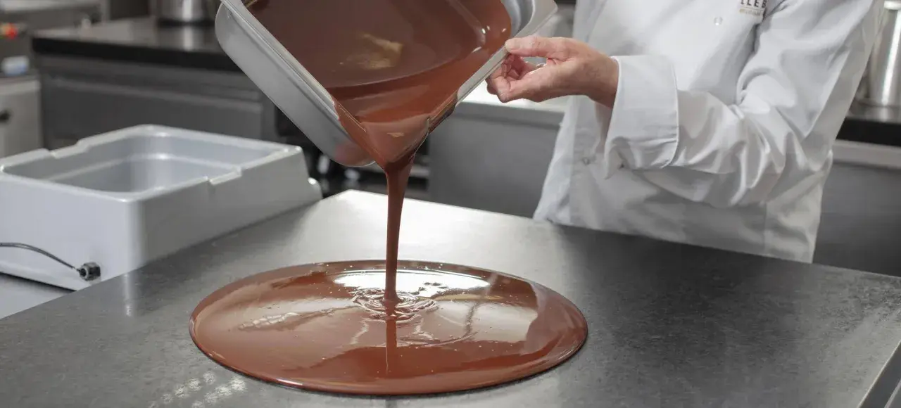 Un chef verse du chocolat fondu, illustrant la différence entre le beurre de cacao et le mycryo pour un tempérage parfait.
