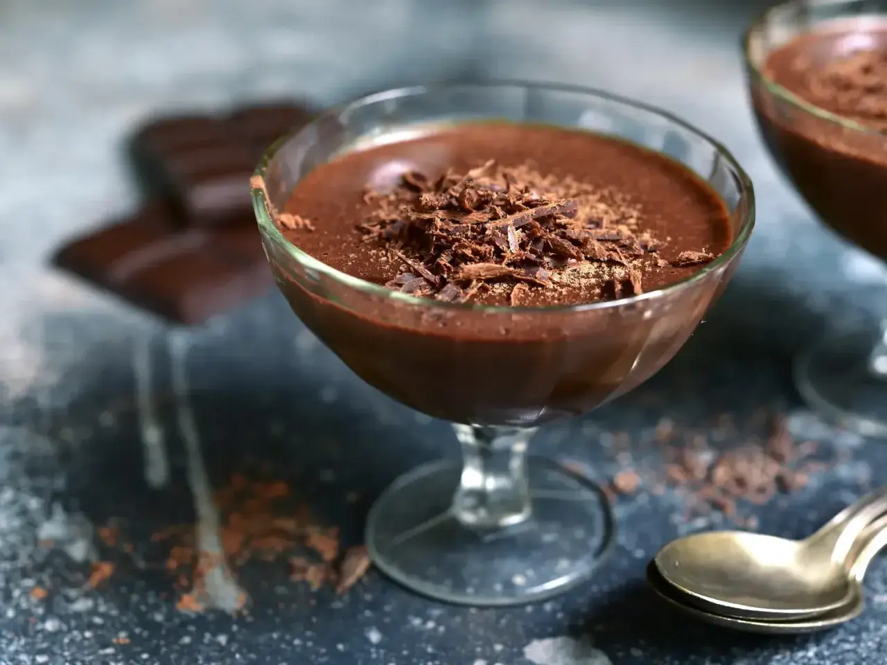 Délicieuse mousse chocolat entremet, garnie de copeaux de chocolat, servie dans un verre. Des carrés de chocolat sont flous en arrière-plan.