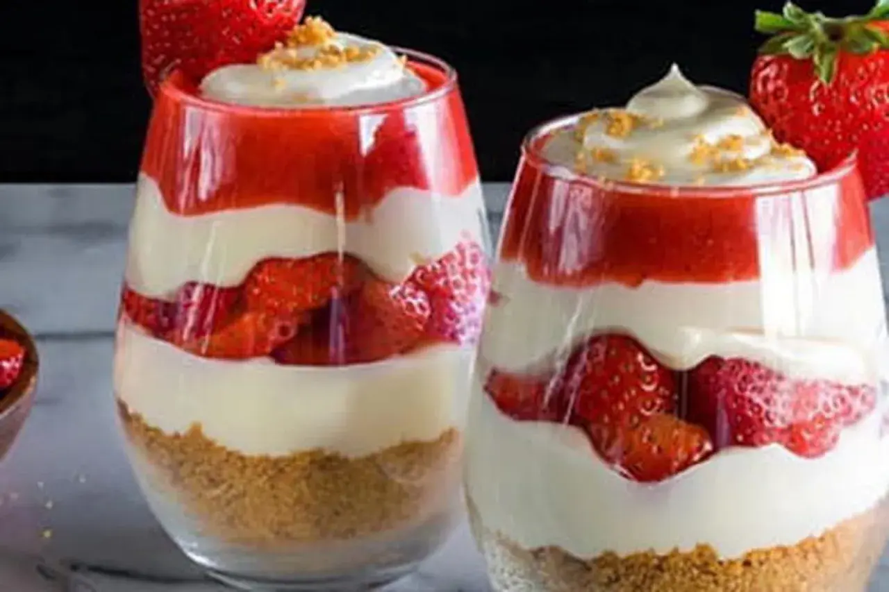 Deux verrines de gâteau fraise crème pâtissière, superposant biscuits émiettés, fraises fraîches, crème pâtissière onctueuse et coulis de fraises.